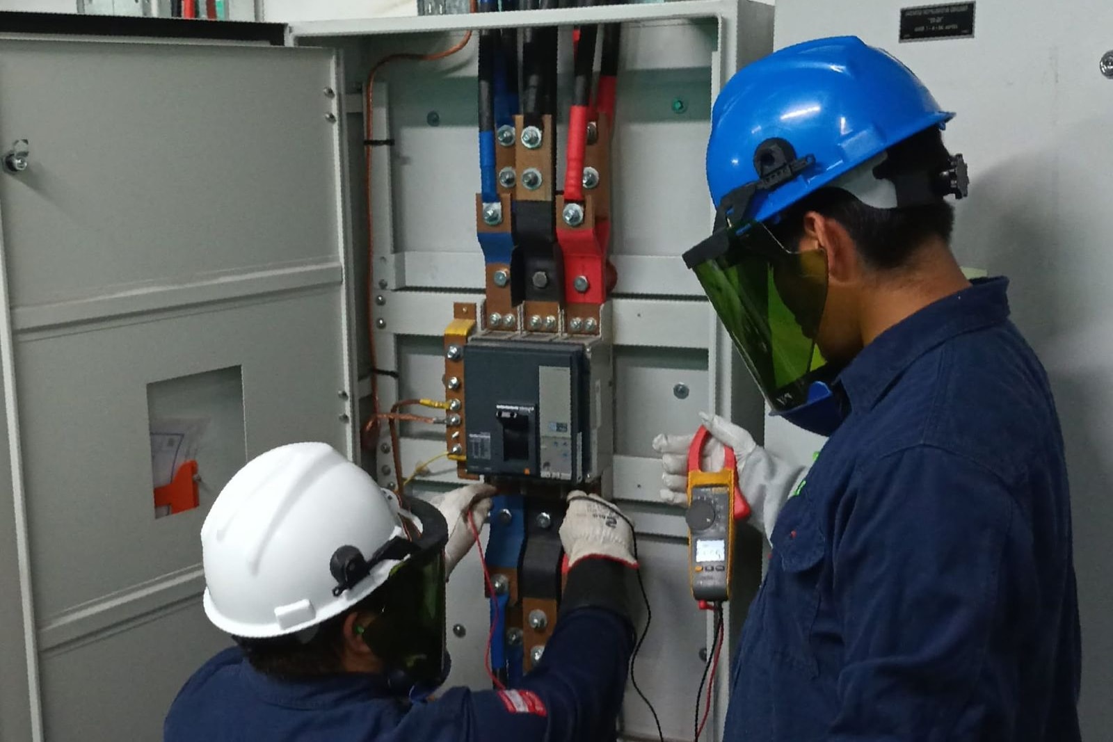Dos técnicos de Master Job con careta de arco y guantes dieléctricos midiendo con pinza amperimétrica en un tablero de distribución.